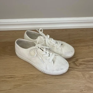 Vita sneakers från NA-KD - Klassiska vita sneakers från NA-KD i tygmaterial, med rund tå och platt sula. Skorna har snörning och en stilren, enkel design som passar till det mesta. Perfekta för dig som gillar en clean och avslappnad look. De är lite smutsiga men är nästan helt oanvända och går lätt att trätta! Priset går att diskutera 