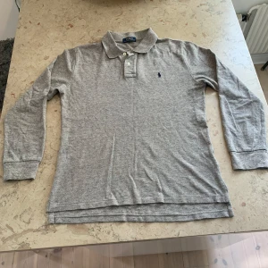 Grå långärmad pikétröja Polo Ralph Lauren - Säljer en klassisk grå långärmad pikétröja från Polo Ralph Lauren. En krage och Ralph lauren loggan broderad på bröstet. Topp skick och inga defekter. Storlek S men passar också XS. 