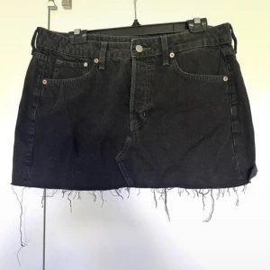 Svart jeanskjol - Svart jeanskjol från &Denim i klassisk femficksmodell med rå, fransig kant nedtill. Kjolen har knapp och dragkedja framtill samt bälteshällor. Perfekt för dig som gillar en edgy och avslappnad stil.