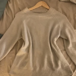 Beige stickad tröja från Vero Moda - Mysig beige stickad tröja från Vero Moda i storlek S. Tröjan har rund halsringning, långa ärmar och ribbade muddar vid hals, ärmslut och nederkant. Perfekt för lager-på-lager och enkel att matcha med jeans eller kjol.