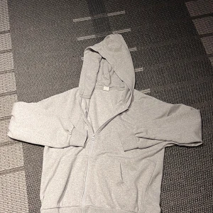 Grå hoodie med dragkedja från Lindex - Enkel och stilren grå hoodie från Lindex i storlek 170. Tröjan har dragkedja framtill, huva och två fickor. Perfekt för chill dagar eller när du vill ha något bekvämt. Tillverkad i mjuk bomullsmix för skön känsla.
