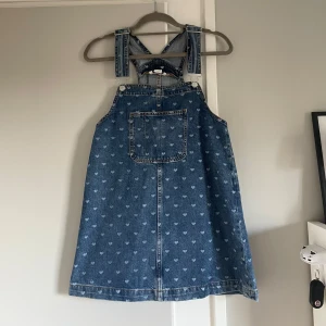 Jeansklänning med hjärtan från Monki - Supersöt jeansklänning från Monki i storlek XS. Klänningen är blå med ljusa hjärtan som mönster, har breda axelband och en stor ficka framtill. Den har tyvärr aldrig kommit till användning så helt ny  dock saknas tagsen. 