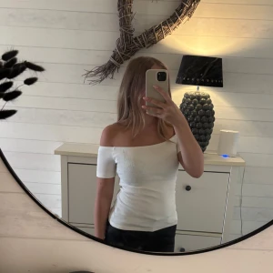 Vit Nelly topp - Säljer en vit, tight offshoulder topp med ribbad struktur. Toppen är använd en gång och kommer från Nelly. Säljer pågrund av att den inte kommer till användning. 