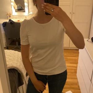 Vit t-shirt med puffärm från Indiska - Snygg vit t-shirt från Indiska med puffade axlar och rund halsringning. T-shirten är i mjuk bomull och har en klassisk passform med korta ärmar. Perfekt att matcha med jeans eller kjol för en clean look. Helt ny,  lappen sitter kvar💕