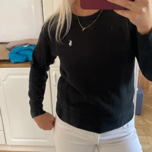 Svart sweatshirt från Polo Ralph Lauren - Klassisk svart sweatshirt från Polo Ralph Lauren med broderad vit logga på bröstet. Tröjan har rund halsringning, långa ärmar och är gjord i mjuk bomull. Perfekt för en chill och stilren look. Passar en s