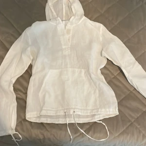 Vit hoodie i linne från Hennes Collection - Vit hoodie i linne från Hennes Collection med huva, känguruficka och snörning nertill. Långärmad och luftig modell som passar perfekt för vår och sommar. Enkel och stilren design som är lätt att matcha med andra plagg.