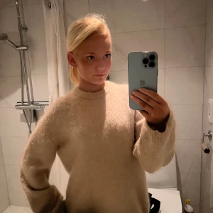 Beige fluffig stickad tröja - Supermysig beige stickad tröja med rund hals och långa ärmar. Tröjan har en fluffig och mjuk känsla, perfekt för kyliga dagar. Enkel och stilren design som är lätt att matcha med jeans eller kjol.