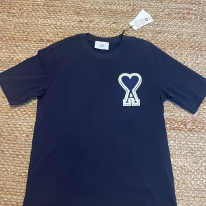 Mörkblå t-shirt från Ami Paris - Snygg mörkblå t-shirt från Ami Paris med broderad logga. Aldrig använd. Säljer pga att den var för stor. Passar medium men även large då den är lite oversized. Priset kan diskuteras. 