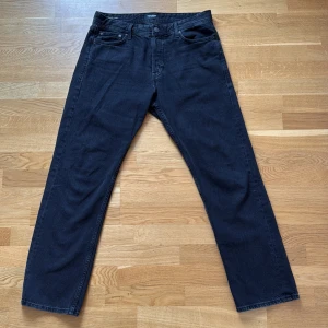 Svarta jeans från Jack & Jones - Säljer ett par svarta jeans från Jack & Jones med klassisk femficksdesign och raka ben. Jeansen har normal passform och är tillverkade i mjukt bomullsmaterial. Perfekt för dig som gillar enkel och stilren look.