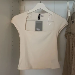 Ribbad vit topp från H&M Divided - Supersnygg ribbad vit topp från H&M Divided med fyrkantig ringning och korta ärmar. Toppens material är mjuk bomullsmix och den har en tight passform som framhäver siluetten. Perfekt att styla med jeans eller kjol för en clean look. Helt ny, ej använd 🩵