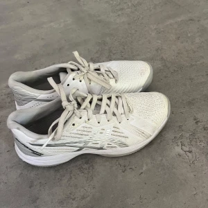 Vita Asics Solution Swift FF Padel - Snygga vita Asics Solution Swift FF Padel-skor med mesh-ovandel för bra ventilation och klassisk Asics-logga i silver. Skorna har snörning, platt sula och mönstrad yttersula för extra grepp på banan. Perfekta för dig som älskar padel och vill ha stilrena skor.