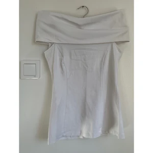 Vit offshoulder topp från Diego Reiga - Snygg vit topp med offshoulder-design och bred krage som kan stylas på olika sätt. Toppen har en figurnära passform. Perfekt för dig som gillar minimalistisk stil med en twist.