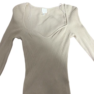 Beige ribbad tröja från H&M - Supersnygg ribbad beige ribbad tröja från H&M med lång ärm och figurnära passform. Tröjan har en markerad byst och bred, fyrkantig ringning som ger en modern vibe. Perfekt för dig som gillar stilrena och trendiga plagg.