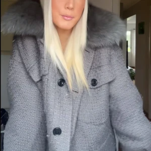 Grå croppad jacka med päls från Meotine - Säljer en grå croppad jacka från Meotine med fluffig päls runt kragen. Jackan har två stora bröstfickor med knappar och grov textur i tyget. Stängs med knappar framtill och har lång ärm. Perfekt för dig som vill ha en cool och trendig look.