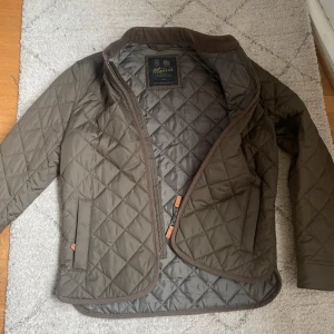  jacka från Morris, olivgrön - Snygg och helt ny jacka från Morris i olivgrön gärg, storlek S. Jackan har ett stilrent rutmönster, dragkedja framtill med läderdetaljer och två fickor. Materialet är polyester och jackan har långärmad passform. Perfekt för dig som gillar klassisk och clean stil.