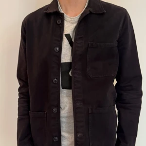 Svart overshirt med fickor från A days march - Snygg svart overshirt med klassisk krage och tre praktiska fickor framtill. Jackan har knäppning med svarta knappar och är långärmad. Materialet är mjukt och känns som bomull, perfekt för lager-på-lager. Enkel och stilren design som funkar till många outfits.