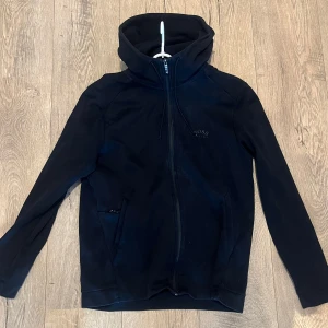 Svart zip hoodie från Hugo Boss - Svart zip hoodie från Hugo Boss med stilren design, huva med snörning och hel dragkedja framtill. Tröjan har diskret logga på bröstet och två sidofickor med dragkedja. Hör av dig för fler bilder eller frågor!