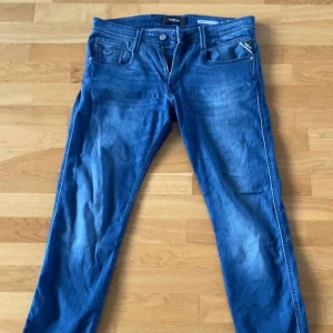 Blå Replay Anbass jeans herr - Snygga blå Replay Anbass jeans med klassisk femficksdesign och tydliga slitningar för en cool look. Jeansen har rak passform och normal midja, med Replay-logga på bakfickan. Perfekta för dig som gillar stilrena och bekväma jeans. W33 L30