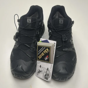Svarta Salomon XA Pro 3D Gore-Tex - Salomon XA Pro 3D sneakers i helsvart med robust design och grov sula för extra grepp. Skorna har snabbsnörning och är tillverkade i slitstarkt syntetmaterial med Gore-Tex-membran som håller fötterna torra. Perfekta för utomhusaktiviteter och äventyr. Aldrig använda.
