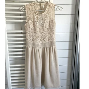 Beige spetsklänning med omlott - Säljer en superfin kortklänning i beige med spets upptill och omlott-detalj i ryggen. 