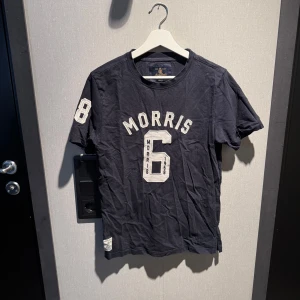 Svart t-shirt Morris med tryck - Svart t-shirt från Morris med stort vitt tryck på bröstet och ärmen. Klassisk rund halsringning och sportig collegekänsla. 