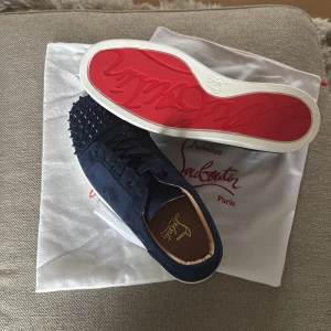Mörkblå Christian Louboutin sneakers med nitar - Snygga mörkblå sneakers från Christian Louboutin i mocka med ikoniska röda sulor och svarta nitar på tån. Helt nya med dustbag, kontakta mig vid fler frågor 