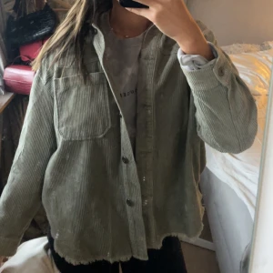 Grön manchester overshirt - Säljer en oversized grön overshirt i manchester med stora bröstfickor och knappar framtill. Jackan har lång ärm, klassisk krage och rå kant nertill för en chill vibe. Perfekt att slänga över en hoodie eller t-shirt.