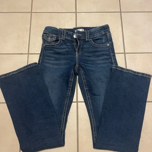 Mörkblå lågmidjade jeans Gina Tricot - Snygga mörkblå jeans från Gina Tricot i storlek 164. Modellen är lågmidjad med kontrastsömmar. Jeansen har bootcut ben och bakfickor med knapp. 