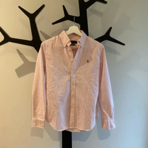 Ralph Lauren Skjorta - Snygg rosa och vit randig skjorta från Ralph Lauren i bomull, custom fit. Klassisk krage, broderad logga på bröstet och knappar framtill. Perfekt för dig som gillar stilrena och fräscha plagg med en preppy vibe.