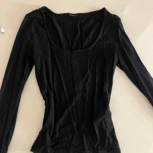 Svart långärmad topp med rund hals - En svart långärmad topp med rundad, djup urringning. Tunn och mjuk i materialet, perfekt att styla med jeans eller kjol. Enkel och stilren design som funkar till många looks.