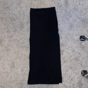 Svart långkjol från Bershka - En svart långkjol från Bershka i enkel och stilren design. Kjolen är rak i modellen och har en liten slits på sidan för extra rörelsefrihet. Perfekt att styla med sneakers eller boots för en cool look.