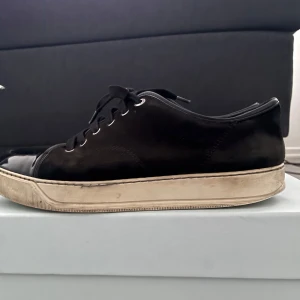 Svarta sneakers från Lanvin i skinn och mocka - Snygga svarta sneakers från Lanvin med ovandel i både skinn och mocka. Klassisk rund tå, svarta snören och vit platt sula med logga undertill. Perfekta för dig som gillar stilrena och lyxiga detaljer. Skorna levereras med original dustbag. Tveka inte på att höra av er vid frågor eller funderingar. Kvitto finns. Pris kan diskuteras vid snabb affär.