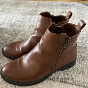 Bruna boots från Alley, storlek 37 - Snygga bruna boots från Alley i storlek 37. Skorna har rund tå, låg klack och dragkedja på sidan för enkel påtagning. Tillverkade i skinnimitation med klassisk design och svart sula. Perfekta för höst och vinter.