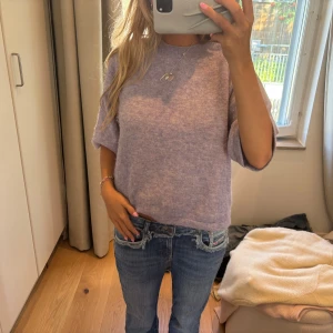 Ljuslila stickad tröja med kort ärm - Supermysig ljuslila stickad tröja med korta, lite vidare ärmar och rund hals. Tröjan har en avslappnad passform och är perfekt att styla med jeans eller kjol. Materialet är mjukt och fluffigt, vilket gör den extra skön att bära.