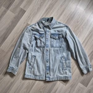Ljusblå jeansjacka med fickor - Snygg ljusblå jeansjacka med klassisk krage och knäppning framtill. Två bröstfickor med lock och knappar samt två sidofickor. Perfekt för lager-på-lager och enkel att styla till olika outfits. Den är baggy. Står xxs men beroende på hur man gillar passformen så passar den upp till cirka L