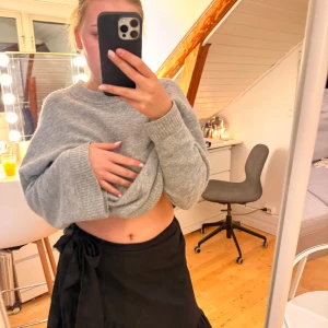 Svart omlottkjol med volang Vero Moda - Supersnygg svart omlottkjol från Vero Moda med volangkant och knyt i midjan. Kjolen är kort och har en flowy känsla som gör den perfekt till en cool och trendig look. Enkel att matcha med både stickade tröjor och crop tops.