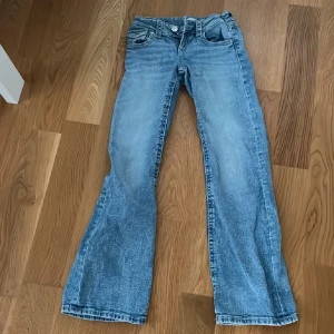 Lågmidjade Blå bootcut jeans från Gina Young str 152 - Säljer ett par snygga lågmidjade blå bootcut jeans från Gina Tricot str 152. De har en klassisk femficksdesign med knapp och dragkedja framtill. Perfekta för en avslappnad stil.