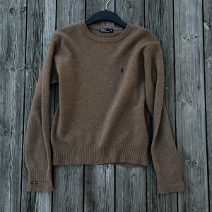 Brun lammullströja från Polo Ralph Lauren - Säljer en klassisk brun stickad tröja från Polo Ralph Lauren. Tröjan har en rund halsringning och långa ärmar med ribbade muddar. Perfekt för kyligare vårkvällar och en enkel look. Storlek M för damer. Några små defekter och därav priset. Hör av dig vid funderingar 