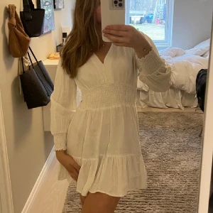 Vit klänning med v-ringning - Vit klänning med v-ringning och långa ärmar från zara. Den har en smockad midja och ger en väldigt fin passform. Perfekt under sommaren ! skriv vid frågor💕