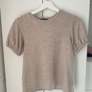 Beige kortärmad tröja från Zara - Säljer en stilren beige tröja från Zara med korta puffärmar. Perfekt för en avslappnad look. Tröjan är tillverkad i ett mjukt material som känns skönt mot huden. Är i storlek M men passar mig som vanligtvis har S eller XS💗