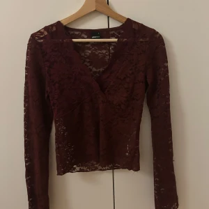 Vinröd spetsblus från Gina Tricot - Snygg vinröd spetsblus från Gina Tricot med långärmad design och v-ringning. Perfekt för en elegant look med sitt genombrutna spetsmönster.