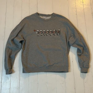 Grå sweatshirt från Polar Skate Co. - Säljer en grå sweatshirt från Polar Skate Co. med ett coolt tryck av en tecknad figur som spelar basket. Tröjan har rund hals och långa ärmar, perfekt för en avslappnad stil. Passar bra för skate men också till vardag!