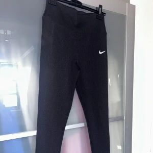 Svarta leggings från Nike - Snygga svarta leggings från Nike med en vit logga på benet. Perfekta för träning eller en avslappnad dag. De har en tight passform och är tillverkade i ett stretchigt material för bästa komfort. Lite tjockare i materialet! Passar M/L