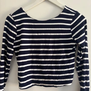 Randig långärmad topp - Säljer en stilren randig topp med långa ärmar. Den har ett klassiskt marinblått och vitt mönster och en rund halsringning. Lite öppen rygg.