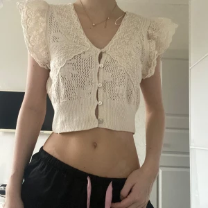 Beige spetsblus med knappar - Säljer en söt beige blus med spetsdetaljer och knappar framtill. Blusen är kortärmad med volangdetaljer och har en croppad passform. Perfekt för en somrig look!