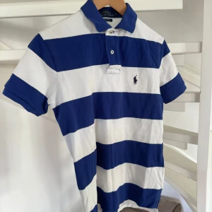 Randig pikétröja från Ralph Lauren storlek S - Säljer min brorsas vit randig pikétröja från Ralph Lauren. Tröjan har korta ärmar och en krage med knappar. Storlek S han kunde ha den när han var runt 171 cm. Använd ett fåtal ggr.