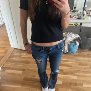 Lågmidjade bootcut jeans med slitningar - Snygga blå bootcut jeans med slitningar från Hollister, de är även utsydda. Säljer då de ej kommer till användning. Midjemått: 39cm rakt över. Innerbenslängd: 79cm. Storlek S skulle jag säga. Använd gärna köp nu!❤️