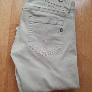 Beiga dondup george jeans - Snygga beige jeansbyxor från Dondup i modellen george⚜️. Byxorna är i storlek 31 och har en slim fit passform📏. Byxorna är tillverkade i bommul och är väldigt sköna och perfekta för en stilren look med fem fickor och knappgylf. Vid frågor eller prisförslag får du mer än gärna skicka ett medelande🤝📬