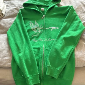 Ak-47 - Säljer en grön hoodie med dragkedja och ett unikt tryck på framsidan. Hoodien har långa ärmar och en bekväm passform. Perfekt för en avslappnad stil.