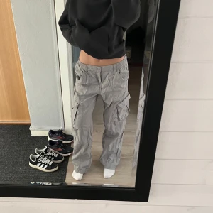 Baggy cargopants - Säljer ett par grå cargopants med flera fickor och en baggy passform. Byxorna har en elastisk midja och är perfekta för en avslappnad stil. De är tillverkade i ett bekvämt material som passar bra för vardagsbruk.